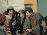 a group of men wearing hats and scarves are standing around a table