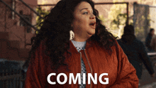 a woman in a red jacket with the word coming behind her