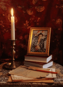 a framed picture of a woman sits on a stack of books next to a lit candle