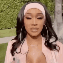 a woman wearing a headband and hoop earrings is standing in front of a bush .