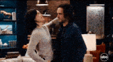 a man and a woman are standing next to each other in a living room with a abc logo on the wall