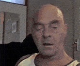 a bald man in a yellow tank top looks at the camera