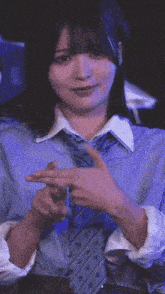 a woman wearing a blue shirt and tie is making a peace sign with her hands