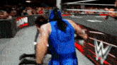 a wrestler in a blue costume is fighting another wrestler in a wrestling ring .
