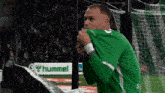 a man in a green shirt stands in front of a hummel advertisement