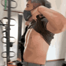 a man wearing a mask is taking off his shirt in a gym .