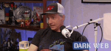 a man is sitting in front of a microphone with a sign that says dark web on it