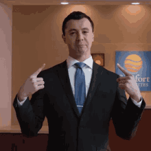 a man in a suit and tie is pointing at himself in front of a sign for comfort suites