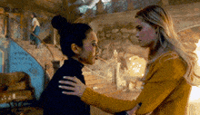 two women are standing next to each other in a room and hugging each other .
