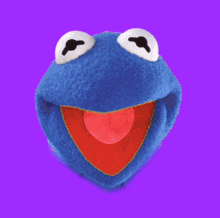 a blue kermit the frog puppet is against a purple backdrop