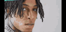 a close up of a man 's face with dreadlocks wearing a hat and a chain around his neck .