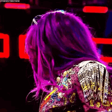 a woman with purple hair is wearing a colorful jacket and looking at the camera .