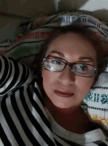 a woman wearing glasses is laying on a bed with a striped shirt on