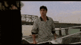 a man in a striped shirt is standing next to a boat and talking to another man .