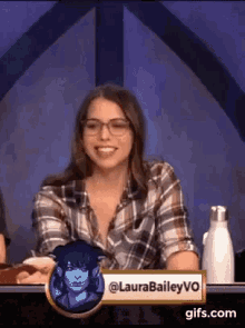 a woman in a plaid shirt and glasses is sitting at a table with a water bottle .