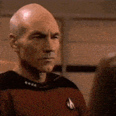 a close up of a bald man wearing a star trek uniform looking at someone .