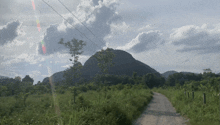 a dirt road leads to a mountain with a cloudy sky