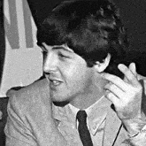 a black and white photo of a man in a suit and tie talking to someone .