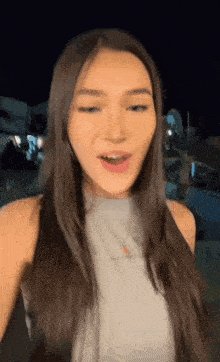 a woman with long brown hair is wearing a gray tank top