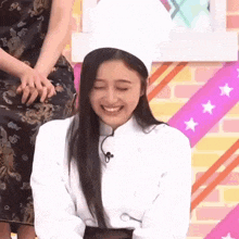 a woman is wearing a chef 's hat and smiling while sitting on a stage .
