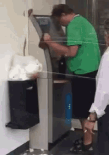 a man in a green shirt stands in front of an atm machine