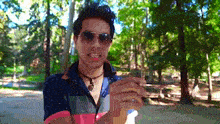 a man wearing sunglasses and a necklace is standing in the woods