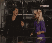 two women are standing in front of a display of handbags and a sign that says pink serije