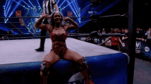 a woman is sitting on the edge of a wrestling ring flexing her muscles
