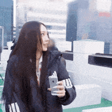 a woman in an adidas jacket is holding a phone