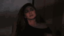 a woman in a black dress is sitting in a dark room looking at the camera .