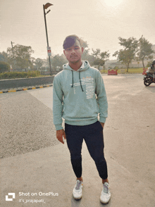 a man wearing a hoodie is standing in a parking lot with the words shot on oneplus written below him