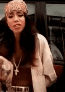 a woman wearing a bandana and a cross necklace is standing in front of a window .