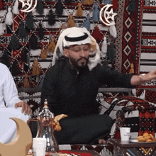 a man wearing a turban sits at a table with a cup that says ' dubai ' on it
