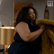 a woman in a black dress is holding a yellow blanket in front of a lamp and a be it logo