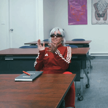 a woman wearing sunglasses and a red adidas jacket sits at a table