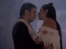 a man in a suit and a woman in a white dress kissing in the rain