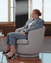 a woman in a blue suit sits in a chair with a glass of water