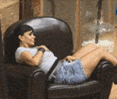 a woman is sitting in a chair with her legs crossed and looking at her phone .