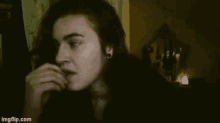 a woman with long black hair is biting her nails while looking at the camera .