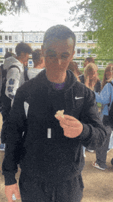a young man wearing a black nike sweatshirt holds a piece of food in his hand