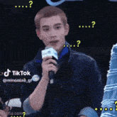 a young man is holding a microphone and has a tiktok sticker on his shirt