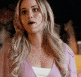 a woman with long blonde hair is wearing a pink cardigan and a white tank top .