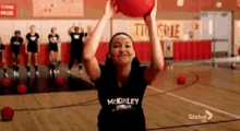 a girl wearing a mckinley shirt is throwing a red ball
