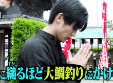 a man in a black shirt is praying in front of a sign that says ' chinese ' on it