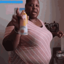 a woman in a pink and white striped shirt is holding a can of orange juice