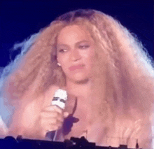 a woman with very long hair is holding a microphone on a stage and making a funny face .