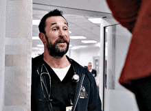 a man with a beard and a stethoscope around his neck is standing next to a wall in a hospital .