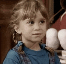 a little girl wearing a blue shirt and plaid overalls looks at the camera