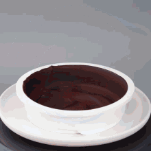 a white bowl filled with dark chocolate sauce on a white plate