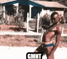 a man in a bathing suit is dancing in front of a house with the word gmnt on the bottom